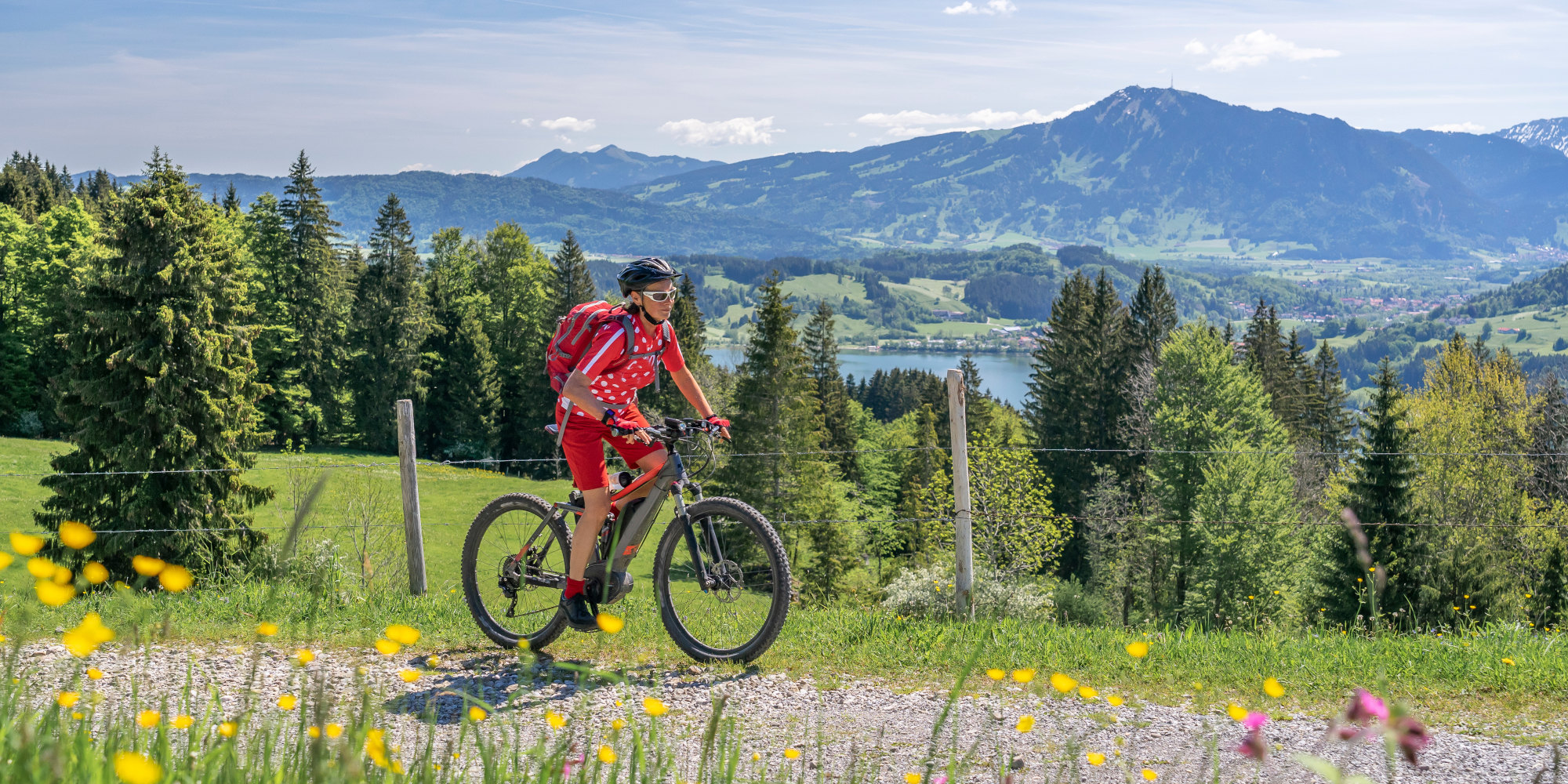 Frau fährt mit einem Fahrrad in den Bergen über dem Alpsee bei Immenstadt