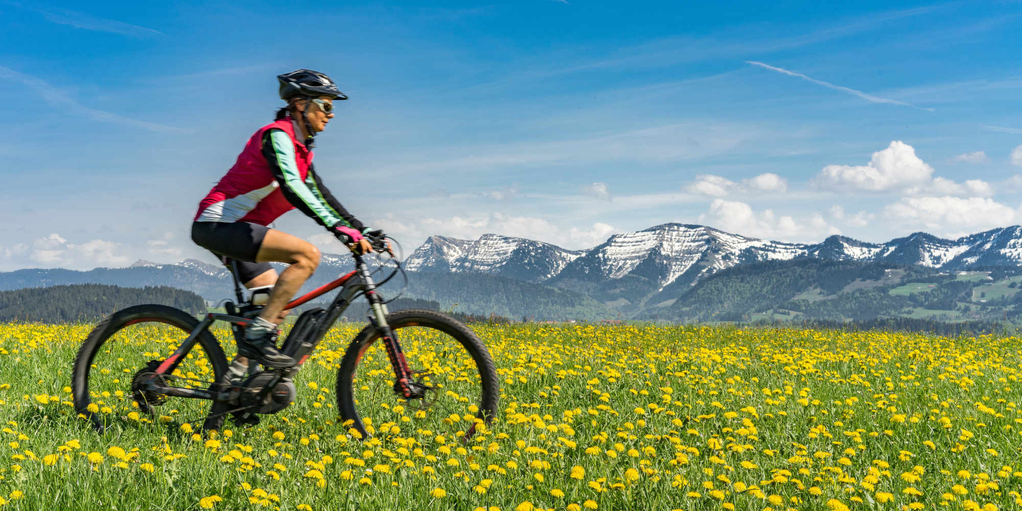 Frau mit Helm fährt mit E-MTB über blühende Wiese.