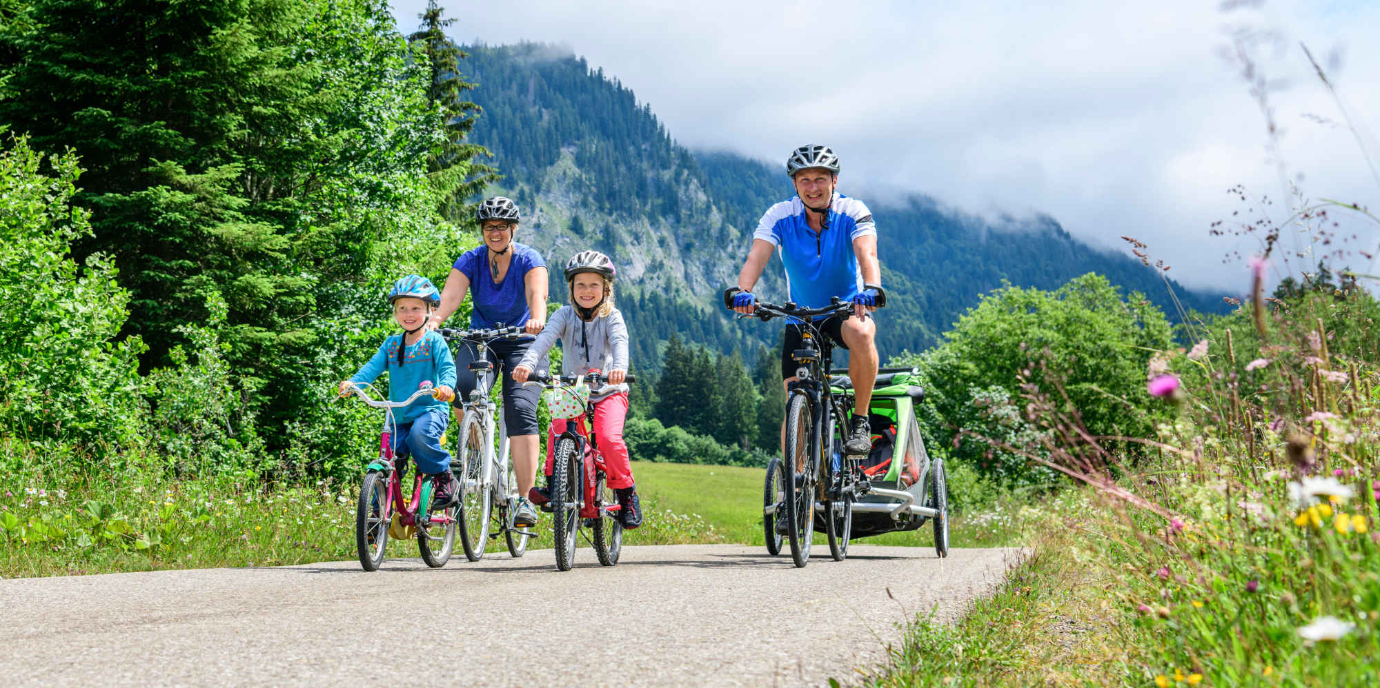 Familie fährt mit Fahrrad und Fahrradanhänger durch die Alpen.