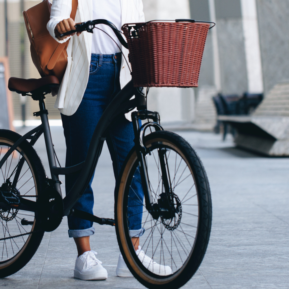 Person steht mit einem Fahrrad in der Stadt, dass einen Fahrradkorb vorne hat.