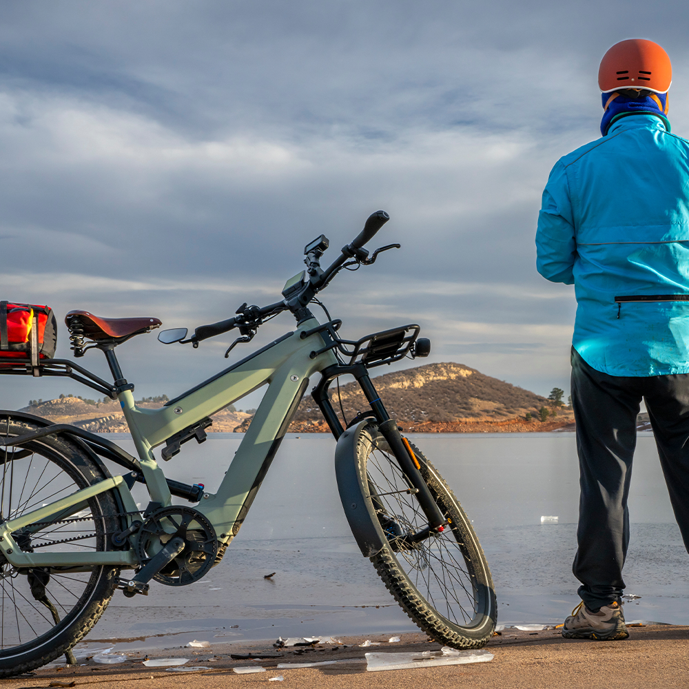 Mann steht mit E-Bike an einem See