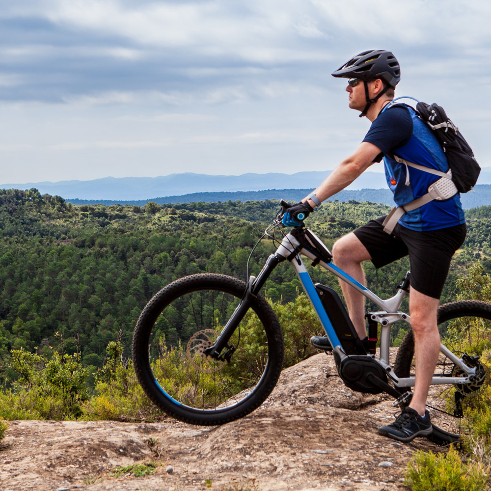 Mann auf einem E-Mountainbike steht auf der Spitze eines Berges.