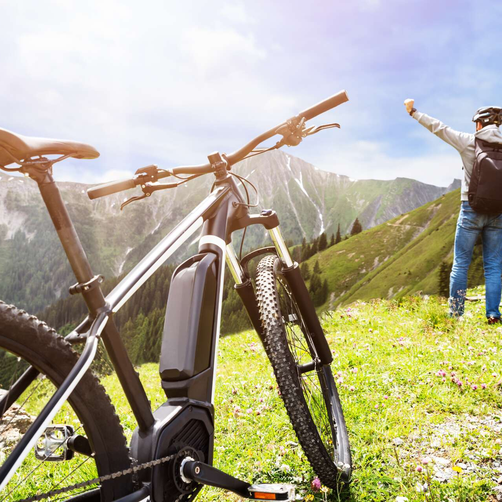 Person steht mit dem Rücken zum Betrachter auf einer grünen Wiese und hebt die arme. Das E-Bike steht im Vordergrund.