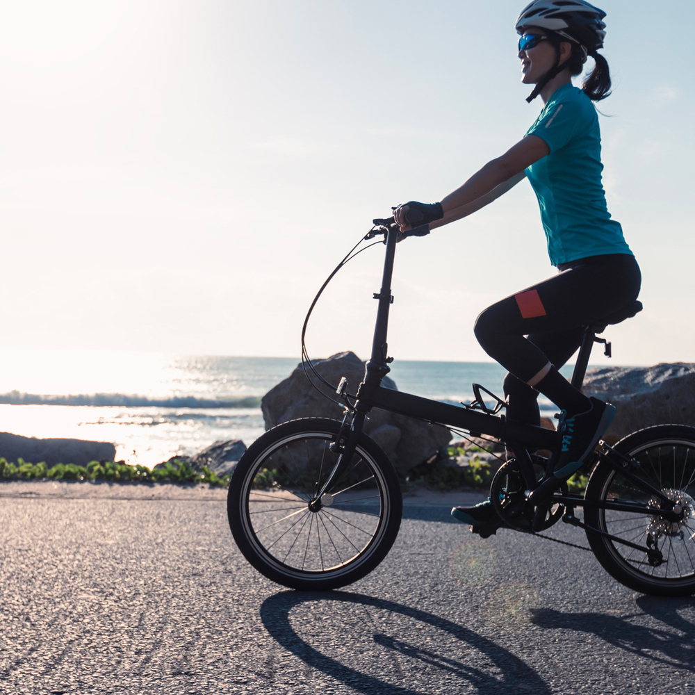 Frau fährt auf einem Klapprad am Meer entlang