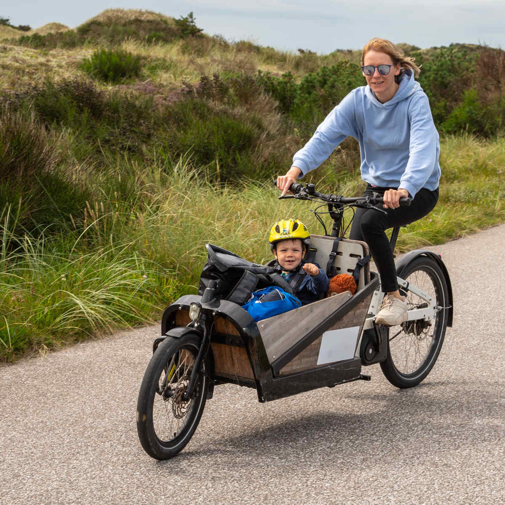 Frau fährt mit Kind im Lastenrad durch Dünen.