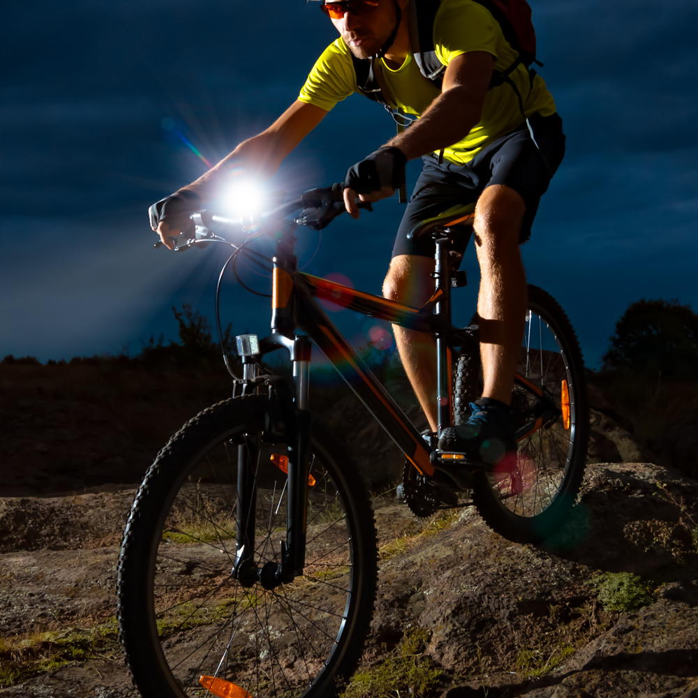 Mann fährt mit dem Fahrrad mit Licht im Dunkeln über einen Berg