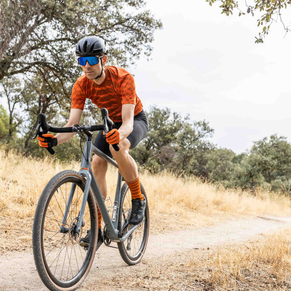 Mann mit Helm fährt auf Gravelbike über einen Weg durch die Natur.