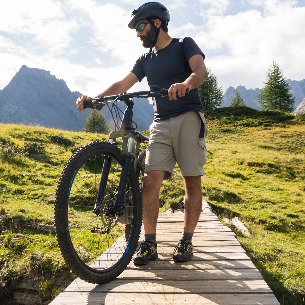 Junger Mann steht auf einer Holzbrücke in der Natur mit einem Fahrrad