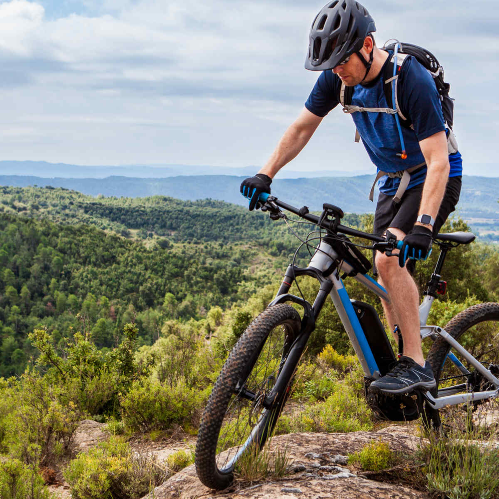 Mann fährt auf E-Mountainbike durch Berge und Wald.