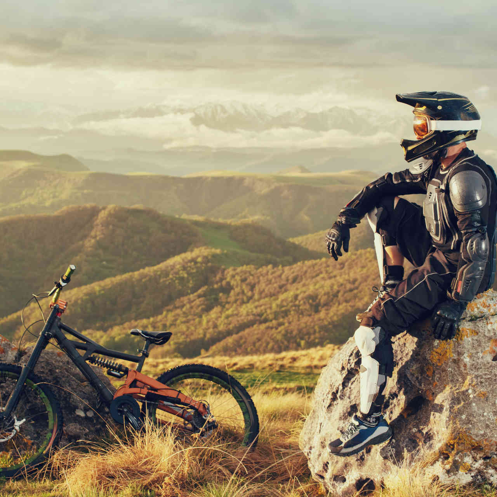 Downhill-Biker sitzt mit Schutzkleidung auf einem Fels