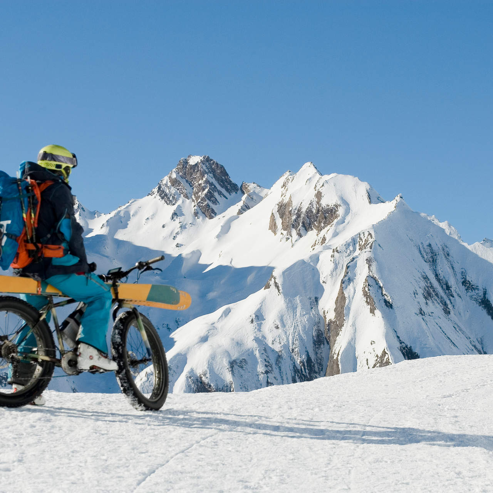 Ein E-Bike Fahrer fährt im Schnee mit seinen Skiern