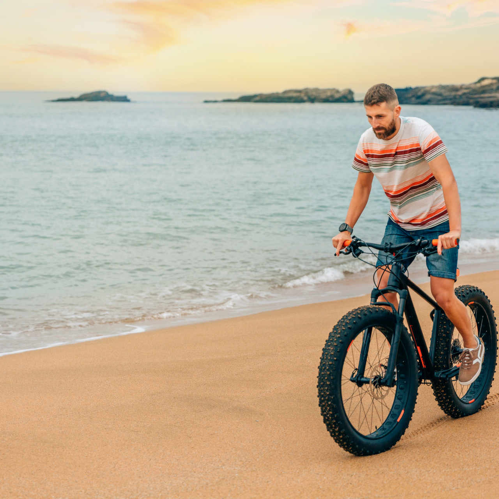 Mann fährt auf Fatbike Strand entlang.