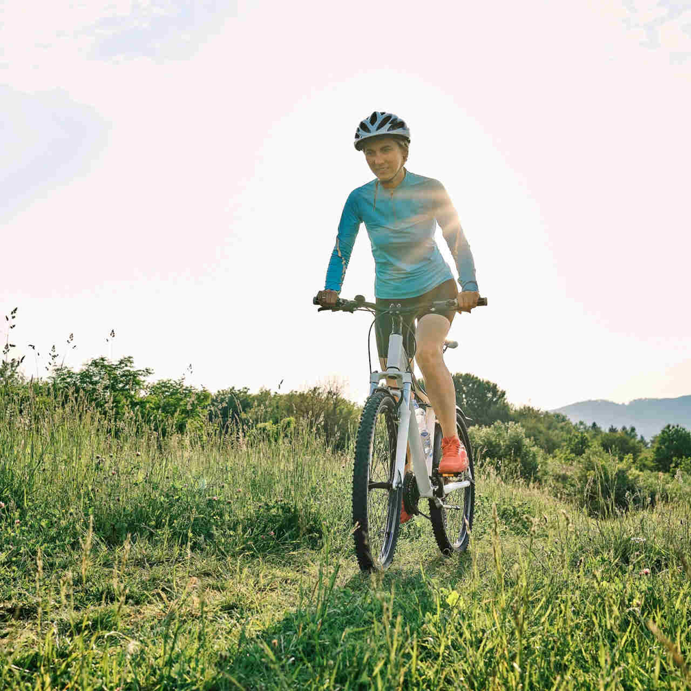 Frau fährt mit Mountainbike über Wiese.